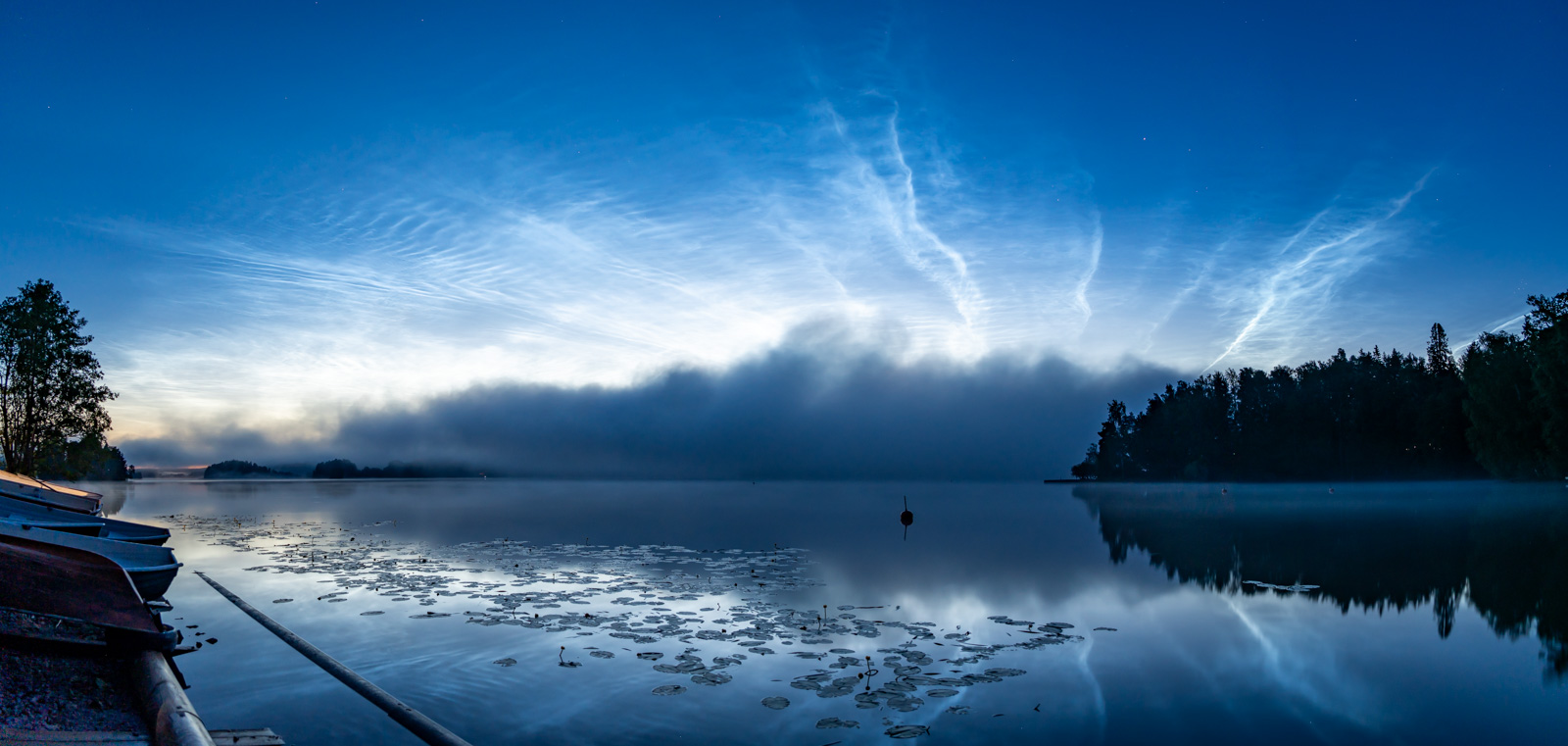 Valaisevat yöpilvet iltausvan peittämällä järvellä